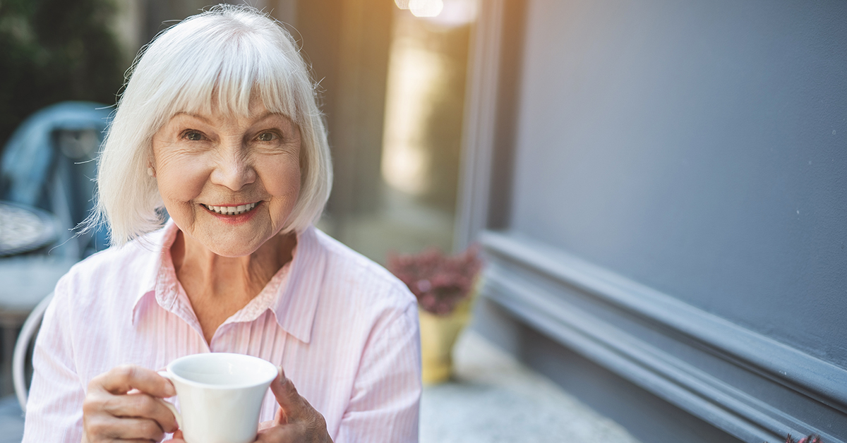 Joyful senior lady having hot drink outdoors
